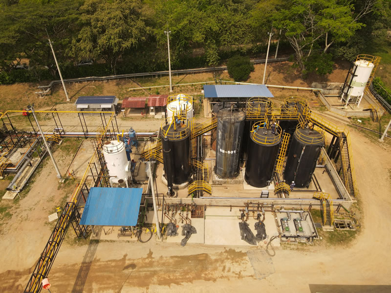 Vista aérea de una facilidad de producción con tanques verticales, pasarelas amarillas y cubiertas azules